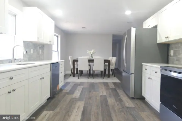 a living room with stainless steel appliances a dining table wooden floor and a view of kitchen