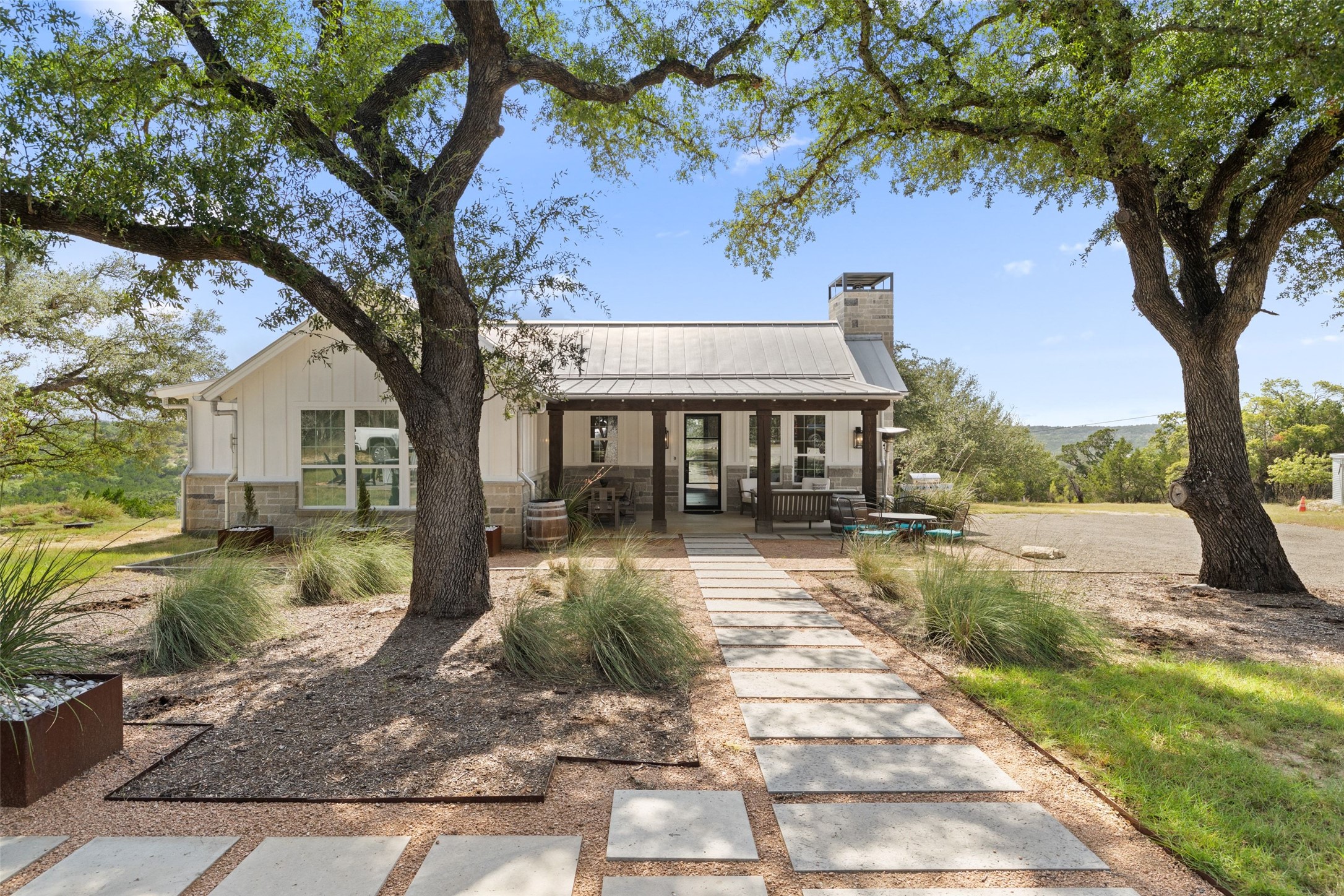 810 Kothmann Road Dripping Springs, TX 78620 - Photo 1 of 40 Mature oak trees frame a modern farmhouse featuring stone accents and a metal roof.