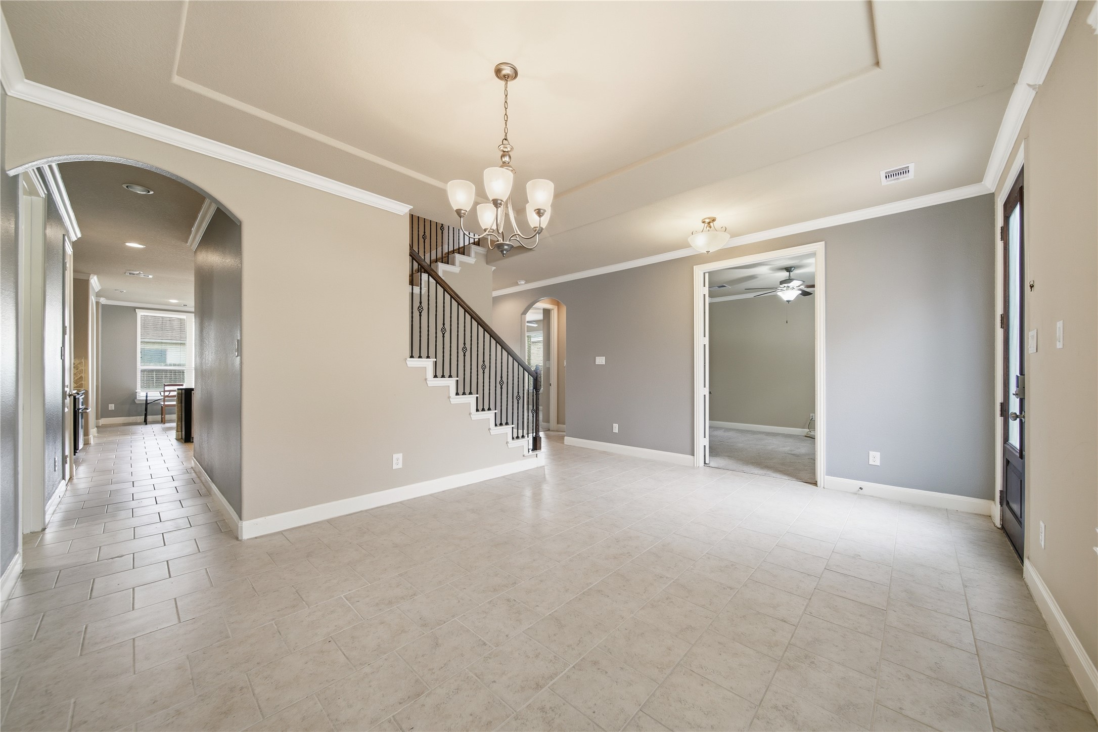 5303 Mesquite Willow Lane Rosharon, TX 77583 - Photo 9 of 32 This spacious, open-concept home features tiled floors, neutral walls, and elegant crown molding. A stylish staircase with wrought iron balusters adds charm, while a modern chandelier enhances the dining area. Ample natural light and an open hallway lead to adjacent rooms, creating a welcoming atmosphere.