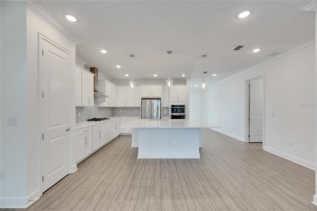 923 Signet Drive Apollo Beach, FL 33572 - Photo 20 of 84 a large white kitchen with kitchen island a sink a stove a refrigerator and white cabinets with wooden floor