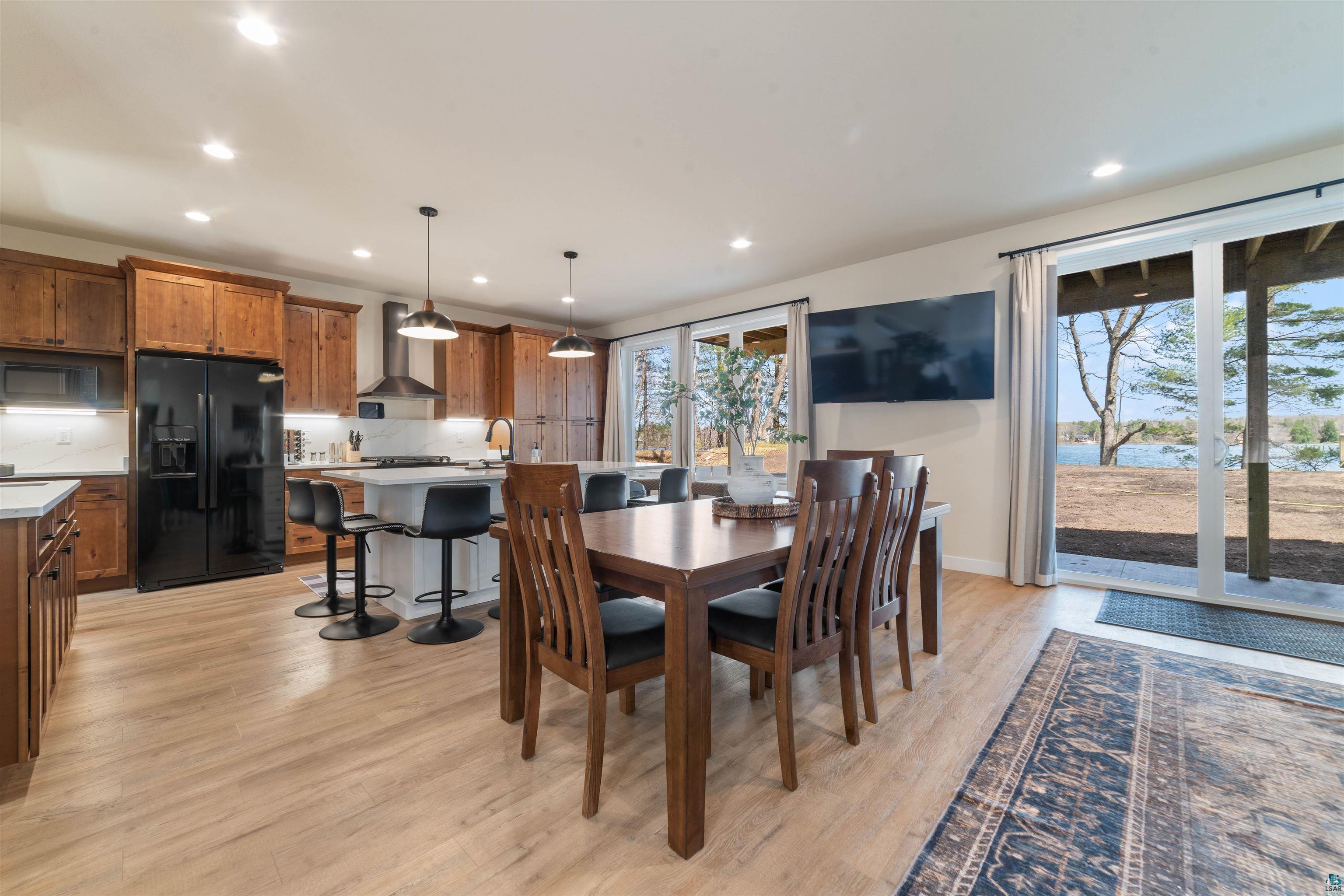2000 West Chub Lake Road Carlton, MN 55718 - Photo 9 of 30 Open-concept living space featuring wood-finish flooring, a kitchen with rich wood cabinetry, a central island with seating, a stainless steel range hood, and sliding glass doors revealing a waterfront setting