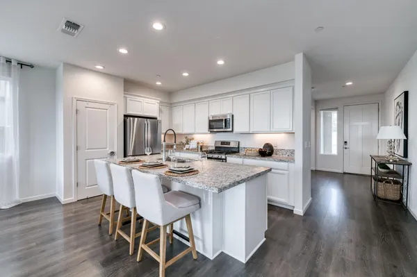 a kitchen with stainless steel appliances granite countertop a stove a refrigerator a sink dishwasher a dining table and chairs with wooden floor