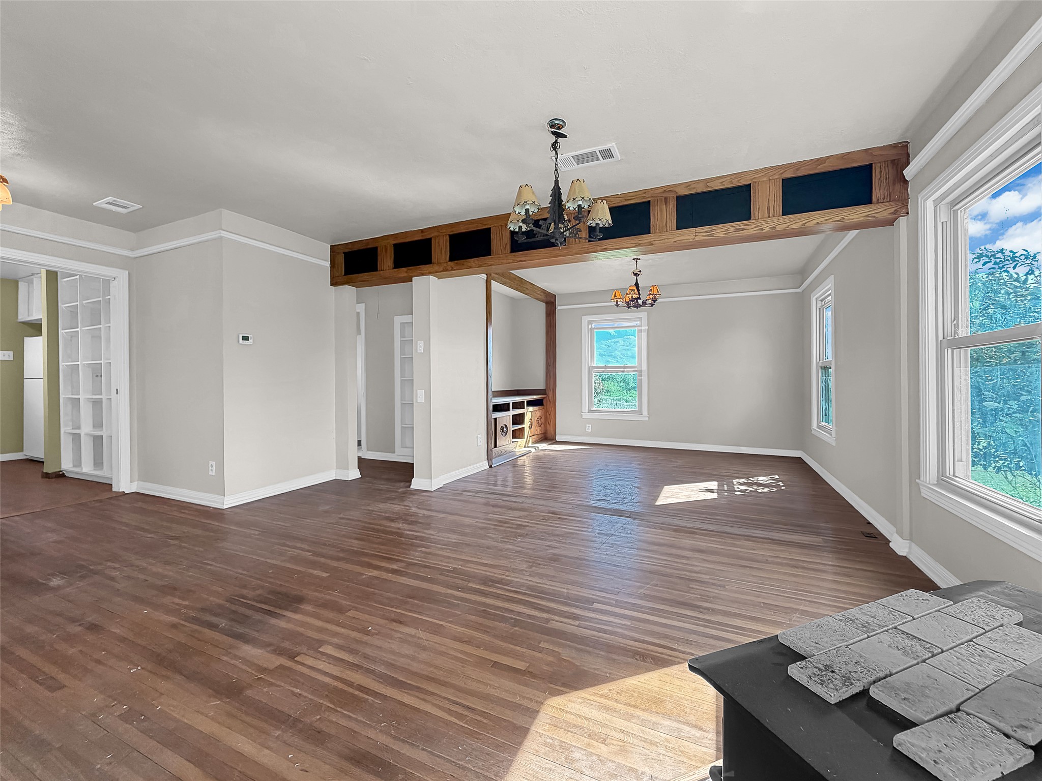 925 Long Hollow Road Dale, TX 78616 - Photo 15 of 26 Spacious room featuring wood-finish flooring, white crown molding, two large windows, a decorative wood beam with recessed panels, and dual chandeliers