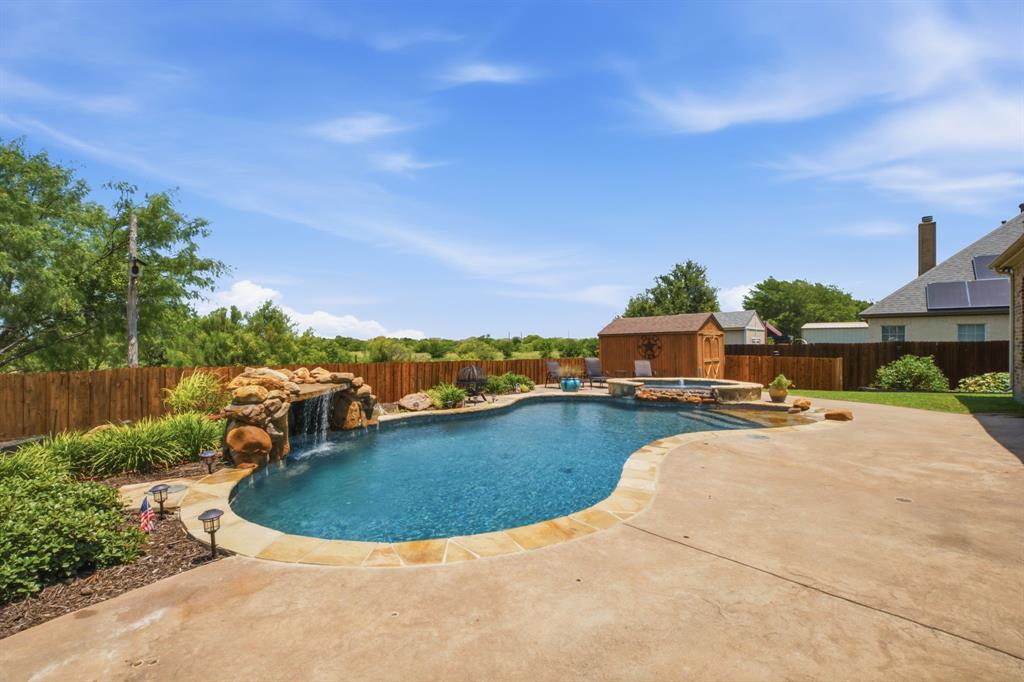 600 Aspen Street Pilot Point, TX 76258 - Photo 33 of 39 Freeform swimming pool with rock waterfall feature, integrated spa, and expansive concrete patio