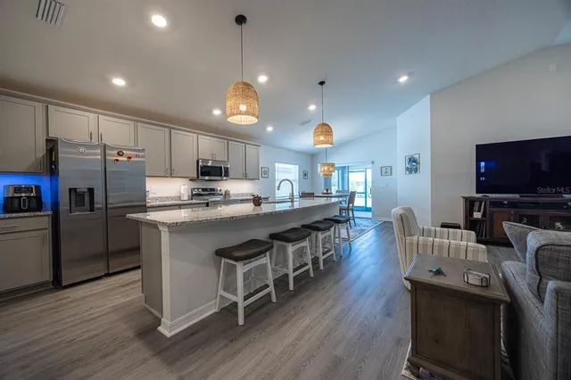 a kitchen with stainless steel appliances a microwave a stove a refrigerator a sink a stove and white cabinets with wooden floor