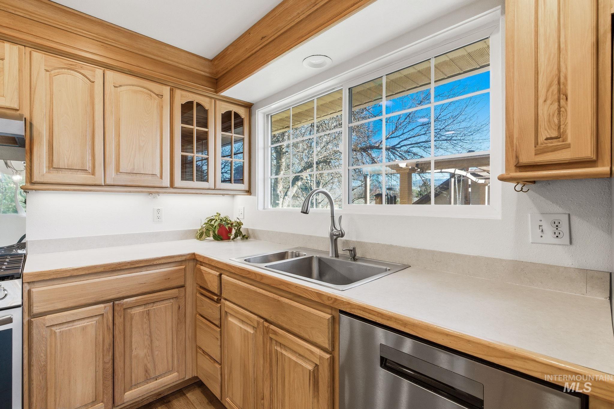 2072 South Crystal Way Boise, ID 83706 - Photo 14 of 50 Kitchen featuring light countertops, dishwasher, light wood finish cabinets, gas range oven, and glass fronted cabinets