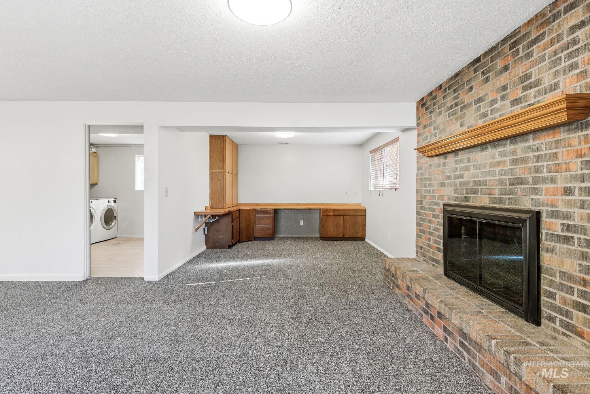 2072 South Crystal Way Boise, ID 83706 - Photo 28 of 50 Unfurnished living room with a brick fireplace, dark carpet, built in desk, washer and clothes dryer, and a textured ceiling