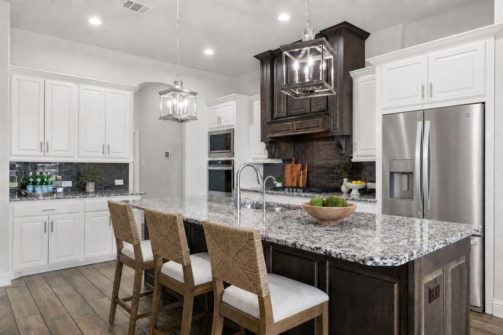 4341 Rush Road Midlothian, TX 76065 - Photo 4 of 39 Open-concept kitchen featuring an oversized island with seating, granite countertops, stainless steel appliances, wood-finish flooring, and pendant lighting fixtures