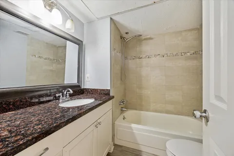 a bathroom with a granite countertop bathtub shower sink vanity and toilet