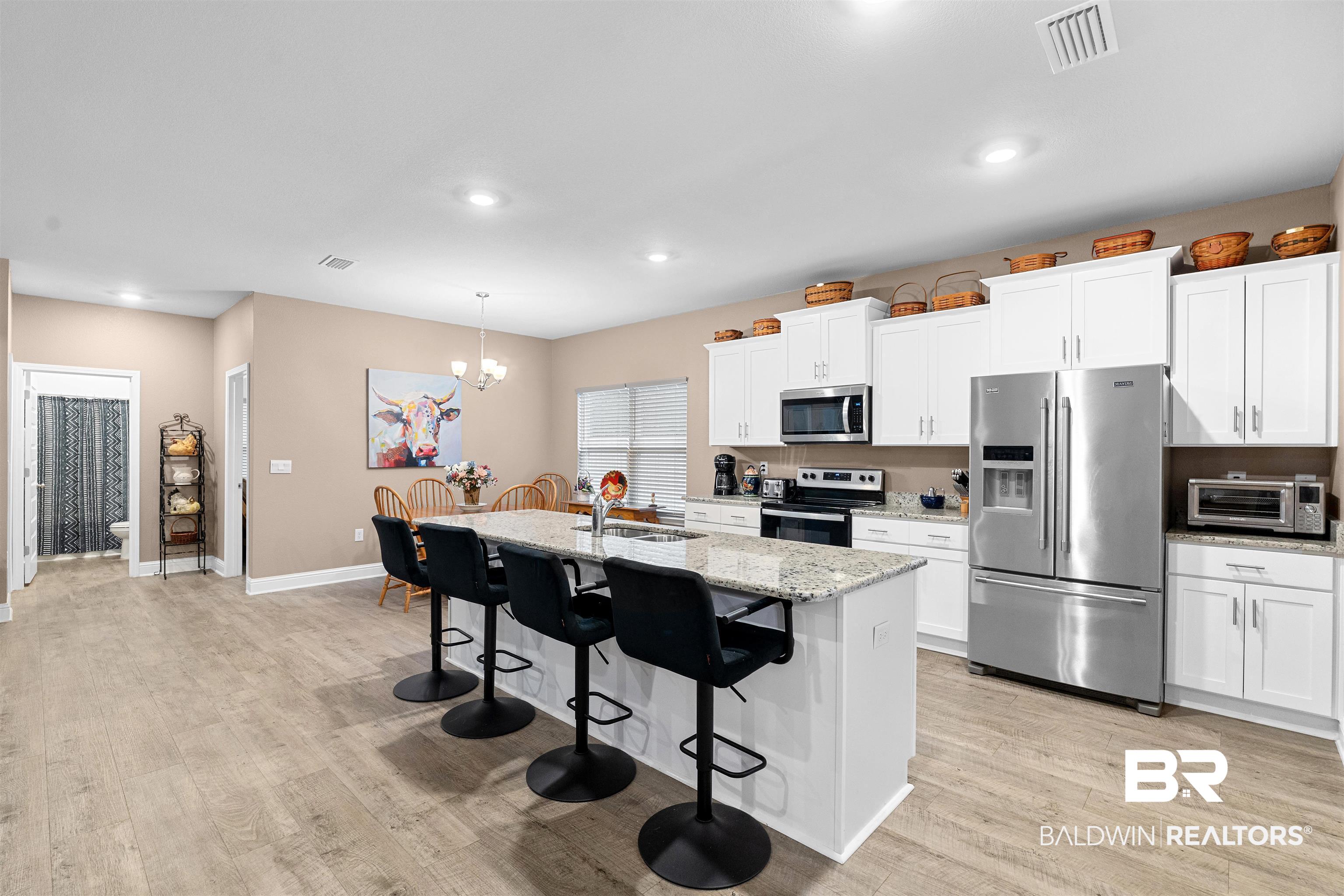 697 Calibre Street Fairhope, AL 36532 - Photo 7 of 18 Kitchen featuring stainless steel appliances, light stone countertops, a kitchen bar, white cabinets, and a center island with sink