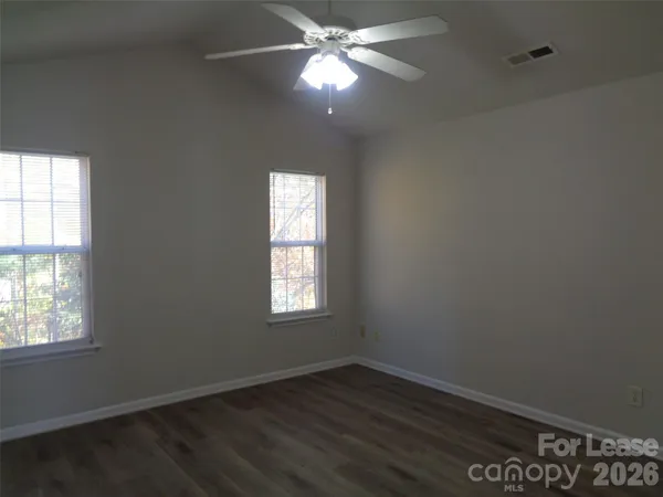 an empty room with wooden floor windows and fan