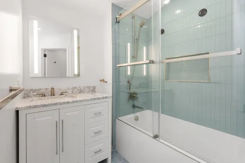 a bathroom with a granite countertop sink a mirror bathtub and shower