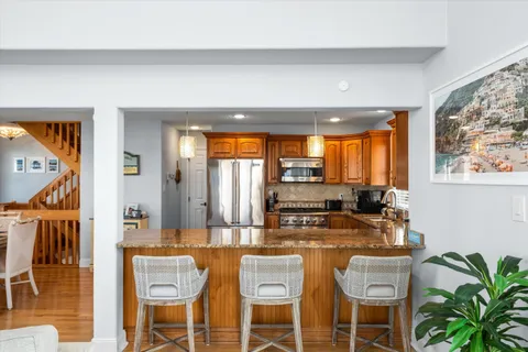 a kitchen with stainless steel appliances a sink a stove a dining table and chairs with wooden floor