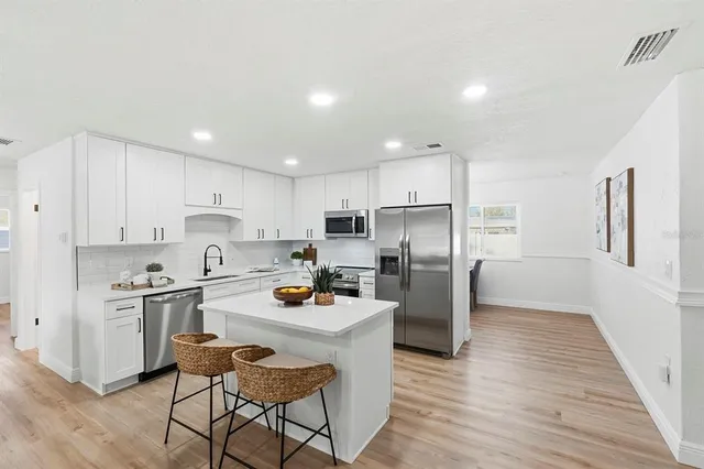 a kitchen with stainless steel appliances a refrigerator a stove a sink dishwasher and white cabinets with wooden floor