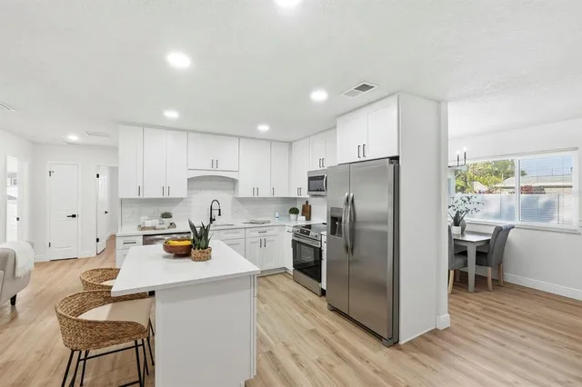 a kitchen with stainless steel appliances a refrigerator a stove a sink a dining table and chairs with wooden floor