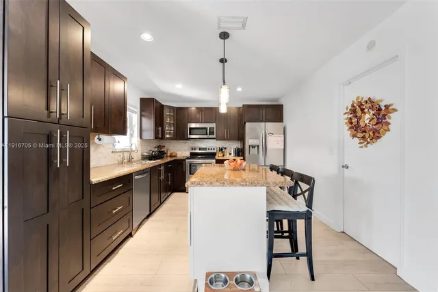 a kitchen with stainless steel appliances kitchen island granite countertop a refrigerator a stove a sink dishwasher a dining table and chairs with wooden floor