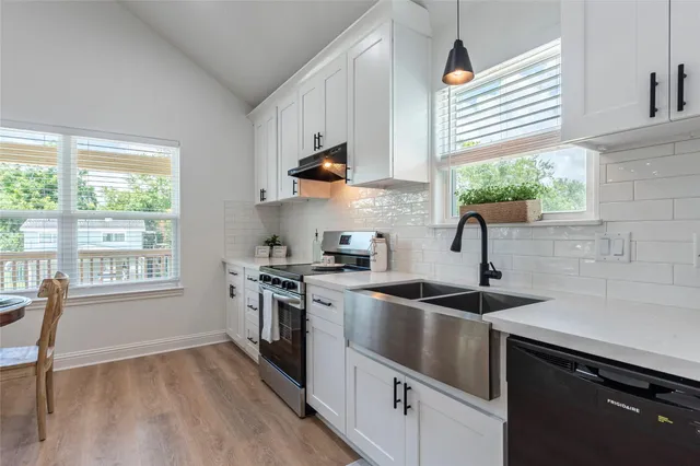 a kitchen with stainless steel appliances kitchen island granite countertop a stove a sink a refrigerator and white cabinets with wooden floor