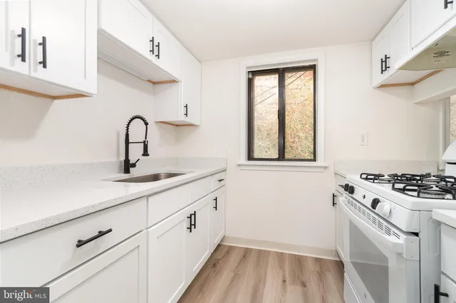a kitchen with white cabinets a sink a stove and wooden floor