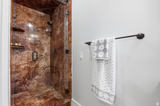 2342 Charros Road Sandy, UT 84092 - Photo 35 of 94 Walk-in shower with brown stone-finish walls and floor, featuring a glass enclosure, built-in shelving, and dark-toned fixtures