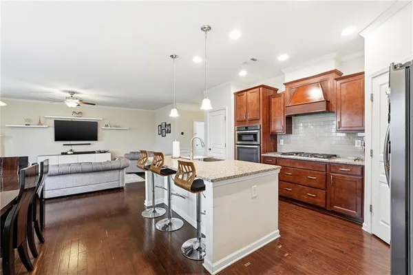 a kitchen with stainless steel appliances granite countertop a stove top oven a sink dishwasher and a refrigerator with wooden floor