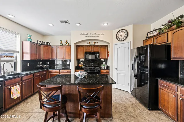 a kitchen with stainless steel appliances granite countertop a stove top oven a refrigerator a sink and chairs