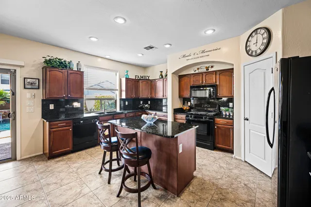 a kitchen with stainless steel appliances granite countertop a refrigerator a stove a sink a dining table and chairs with wooden floor