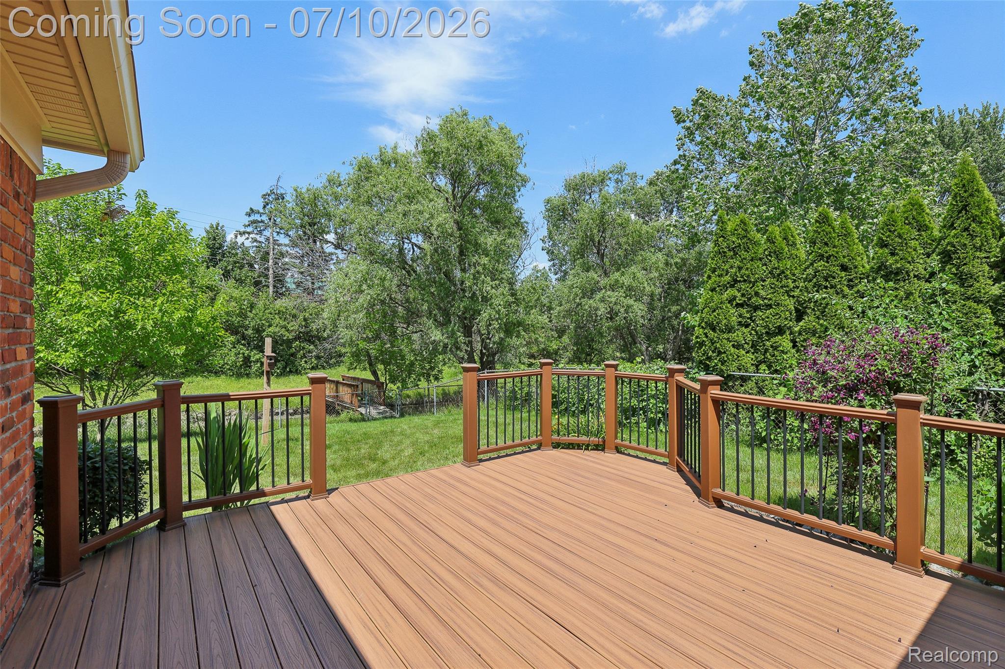 42698 Keystone Canton, MI 48187 - Photo 29 of 33 Spacious outdoor deck featuring composite decking, wood-finish railing with black balusters, and a verdant backdrop of mature trees and shrubs