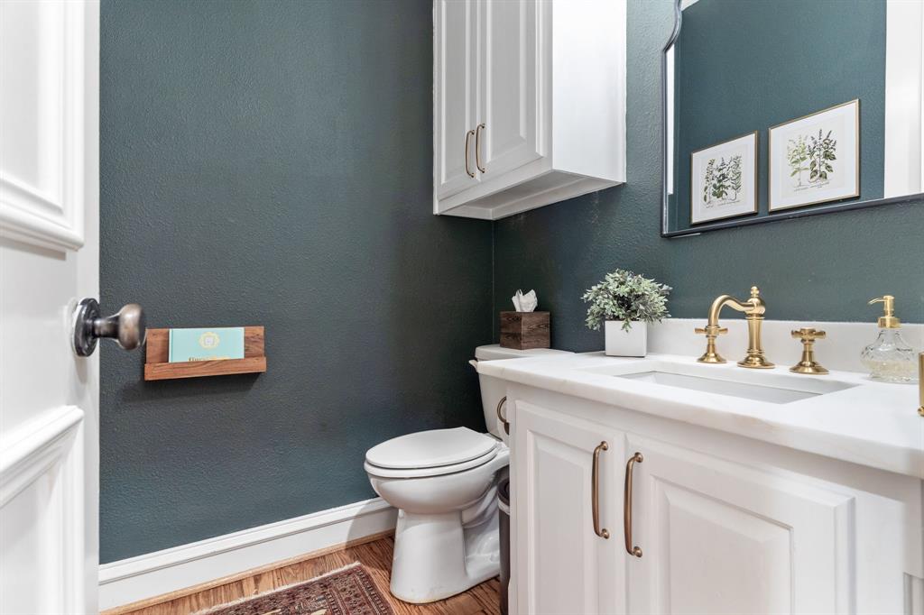 2404 Racheal Drive Heath, TX 75032 - Photo 17 of 40 The first-floor, guest powder bathroom features warm wood floors and a fresh coat of Magnolia-1905 paint. A crisp white built-in vanity, topped with a leathered dolomite countertop installed in 2023, is paired with an under-mount sink, Restoration Hardware faucet, and Anthropologie light fixture. An integrated upper cabinet adds storage, completing this elegant and thoughtfully updated space.