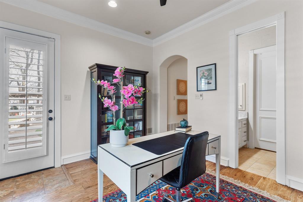 2404 Racheal Drive Heath, TX 75032 - Photo 23 of 40 The first-floor mother-in-law suite offers versatile living, easily serving as a guest retreat or a second home office. Hardwood floors flow beneath two windows with plantation shutters overlooking the pool and spa, while a glass exterior door with matching shutters provides direct backyard access. A black built-in cabinetry and shelving unit cleverly converts into a full-size Murphy bed for guests (stays with the home), complemented by crown molding, a new remote-controlled ceiling fan, and an elegant en suite bathroom.