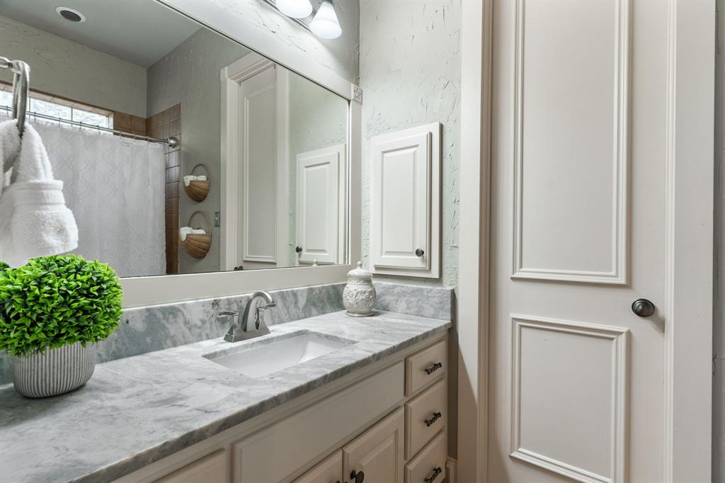 2404 Racheal Drive Heath, TX 75032 - Photo 24 of 40 The mother-in-law or guest en suite bathroom exudes refined style with tile floors and skip-trowel textured walls. A white vanity with black hardware and a marble countertop houses an under-mount sink with brushed nickel fixtures, accompanied by a matching medicine cabinet. The separate shower-tub combination features a tile surround, brushed bronze faucet and showerhead, and an upper window that fills the space with natural light. Completing the suite is a spacious walk-in closet, offering storage for the home or for guests.