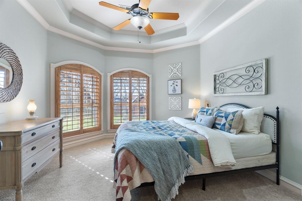 2404 Racheal Drive Heath, TX 75032 - Photo 25 of 40 Bedroom 3, located on the second floor, showcases a distinctive hexagonal design, offering architectural interest and charm. Plush carpeting adds comfort underfoot, while two arched windows with plantation shutters frame views of the front yard. A tray ceiling with double crown molding and a ceiling fan enhances the space, and a walk-in closet with built-in shelving provides ample storage for clothing and accessories.