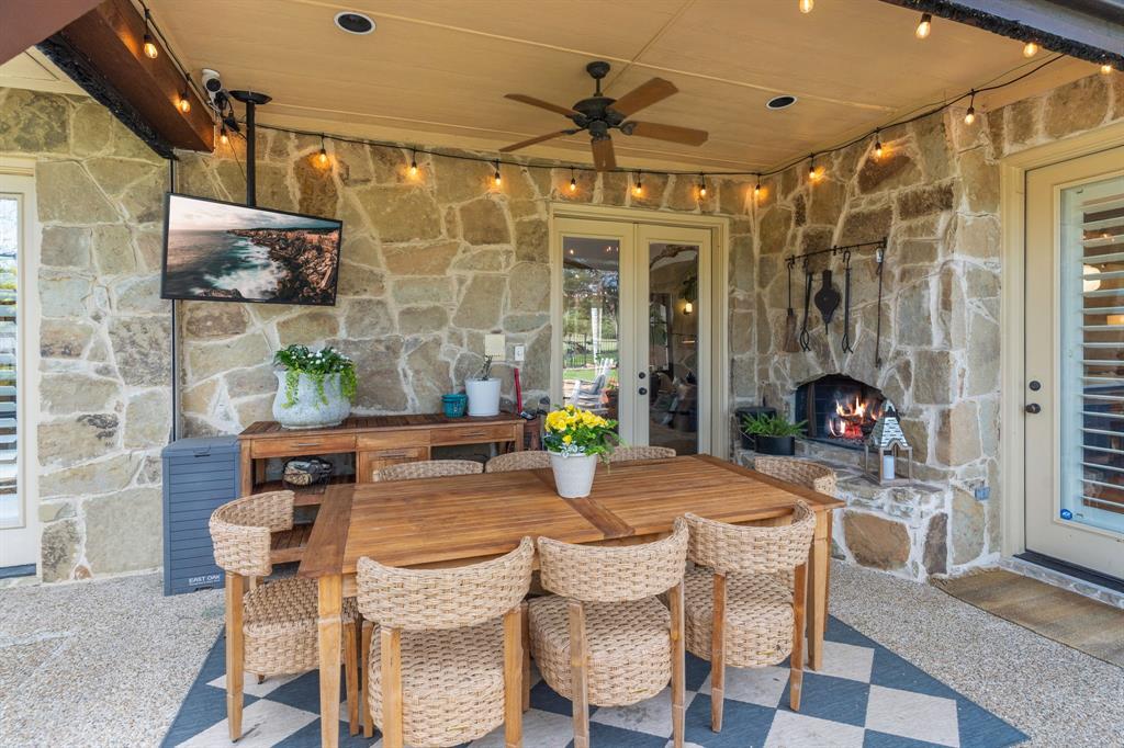 2404 Racheal Drive Heath, TX 75032 - Photo 31 of 40 The covered back porch provides additional living and dining spaces, offering seamless indoor-outdoor flow with three points of access from the primary suite, kitchen, and main entry parlor. Designed for year-round enjoyment and entertainment, the back porch features a stone, gas fireplace with raised hearth, a mounted flat-screen TV, new remote-controlled retractable screens, extensive, new smart string lighting controlled with the Hubspace app, and a ceiling fan for added comfort.