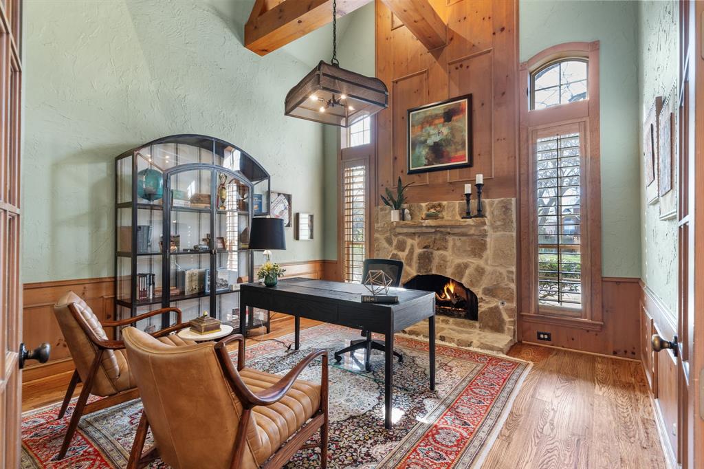 2404 Racheal Drive Heath, TX 75032 - Photo 8 of 40 The stately, private study exudes a warm, moody ambiance, featuring rich pine paneling, skip trowel textured walls, a dramatic floor-to-ceiling gas fireplace with a stone face and mantel, and an unforgettable vaulted ceiling with exposed architectural pine beams anchored by a striking metal chandelier. The study is accessed through glass-paneled French doors, and two windows with matching plantation shutters perfectly complement the room’s sophisticated character.