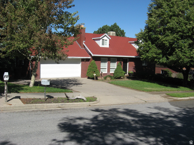 New england style home featuring driveway, a front lawn, an attached garage, and brick siding