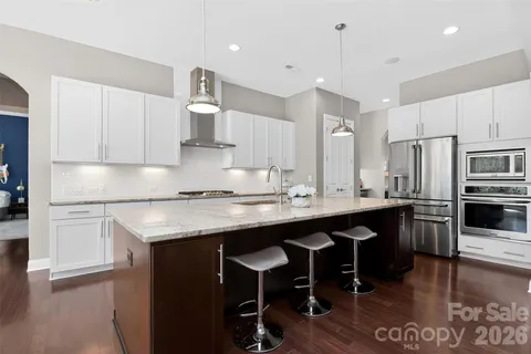a kitchen with stainless steel appliances granite countertop a sink a stove a refrigerator and island with wooden floor