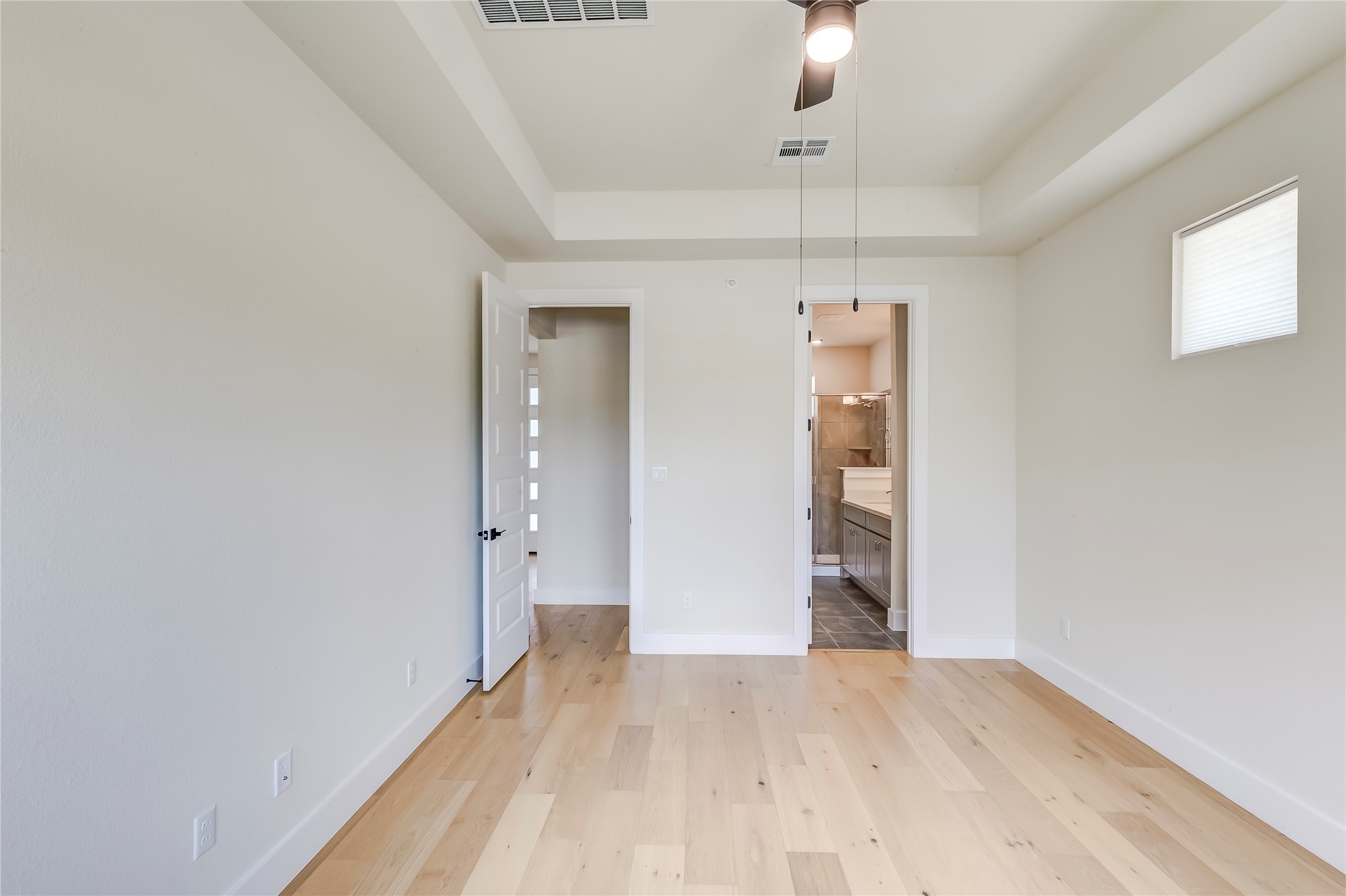 2600 Gattis School Road, Unit 401 Round Rock, TX 78664 - Photo 19 of 29 Unfurnished bedroom with a tray ceiling, light wood finished floors, connected bathroom, and a ceiling fan