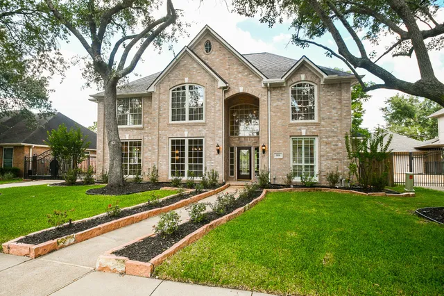 a view of a yard in front of a brick house with plants and large trees