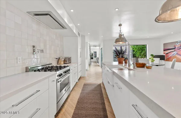 a large kitchen with stainless steel appliances a stove a chimney a sink dishwasher and white cabinets with wooden floor