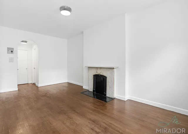 a view of an empty room with wooden floor and a fireplace