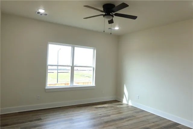 an empty room with wooden floor ceiling fan and windows