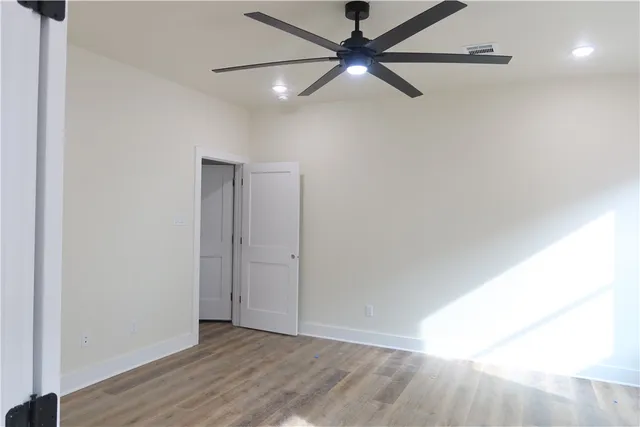 a view of an empty room with wooden floor and a ceiling fan