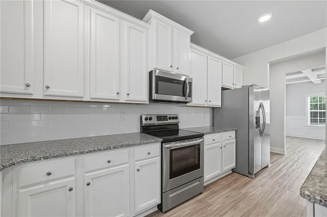 a kitchen with stainless steel appliances granite countertop white cabinets and a stove top oven
