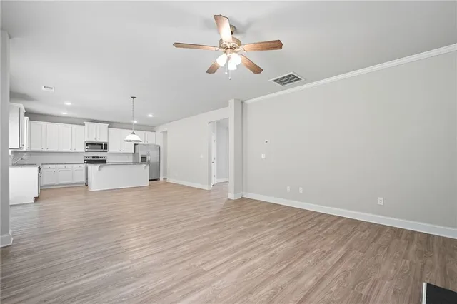 a view of an empty room with wooden floor and a ceiling fan