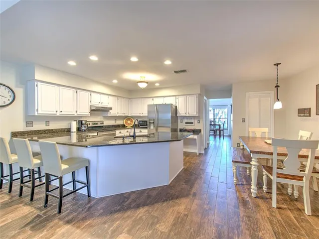 a kitchen with stainless steel appliances granite countertop a stove top oven a sink a dining table and chairs with wooden floor