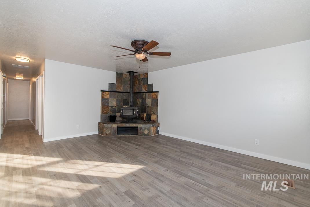 480 Easy Street Kuna, ID 83634 - Photo 24 of 39 Unfurnished living room featuring a wood stove, a ceiling fan, wood finished floors, and a textured ceiling