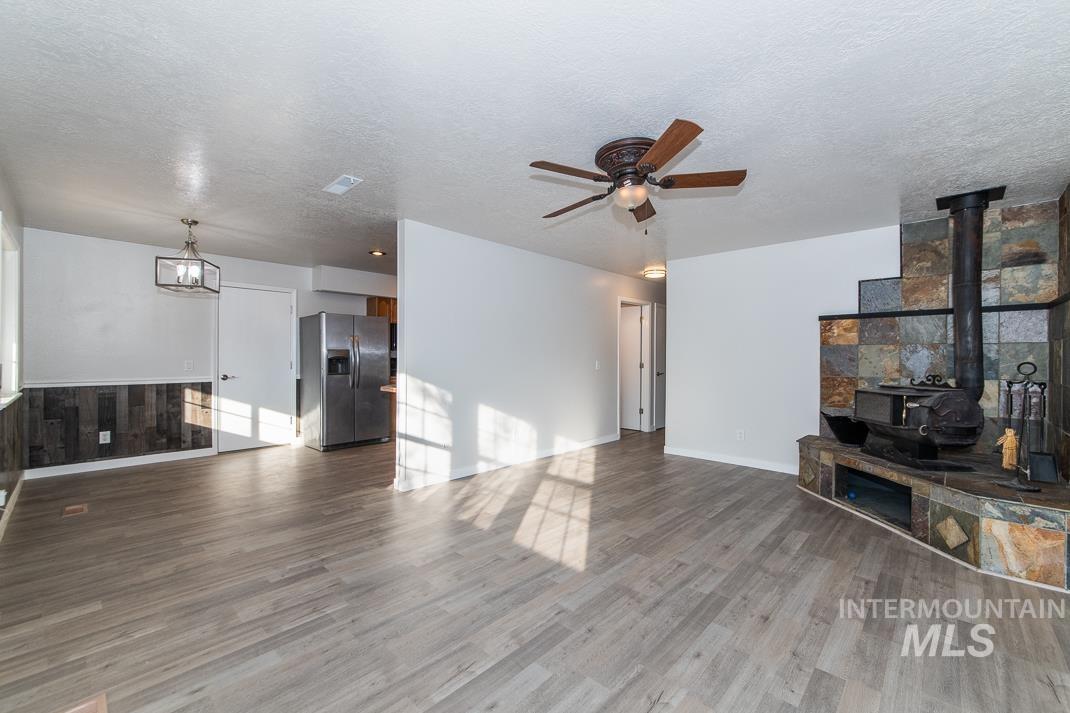 480 Easy Street Kuna, ID 83634 - Photo 25 of 39 Unfurnished living room with a wood stove, light wood-style floors, a ceiling fan, a textured ceiling, and a chandelier