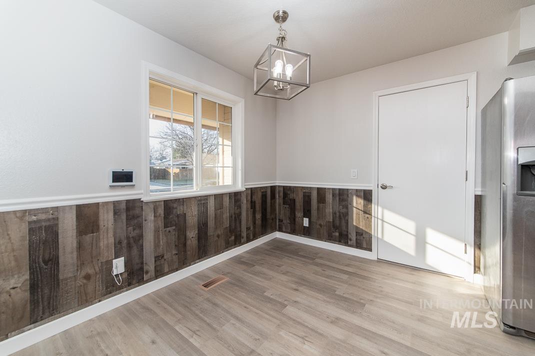 480 Easy Street Kuna, ID 83634 - Photo 27 of 39 Unfurnished dining area featuring wainscoting, wood walls, a chandelier, and light wood-type flooring