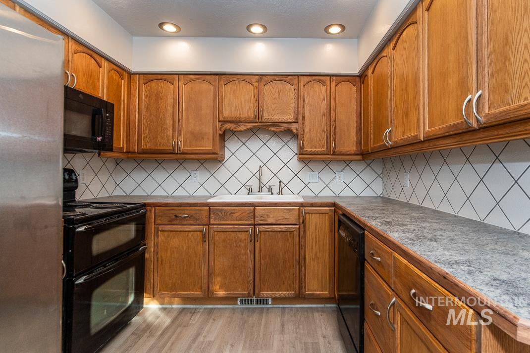 480 Easy Street Kuna, ID 83634 - Photo 28 of 39 Kitchen featuring brown cabinetry, black appliances, light wood-style floors, and tasteful backsplash