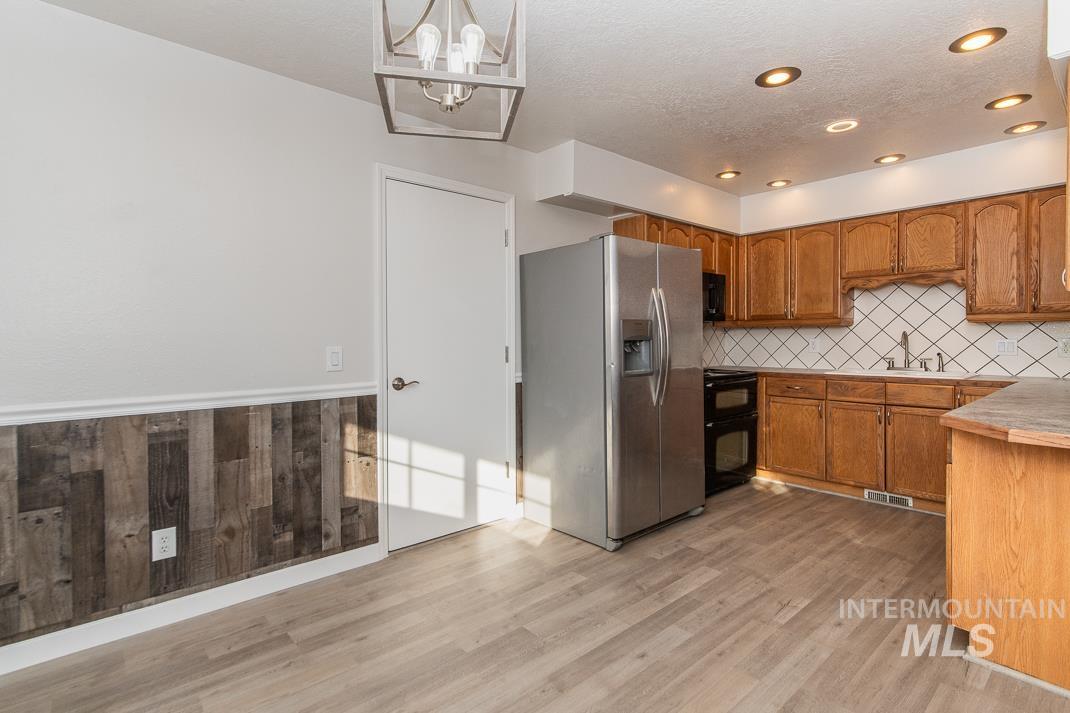 480 Easy Street Kuna, ID 83634 - Photo 31 of 39 Kitchen with black appliances, brown cabinetry, light countertops, wainscoting, and a textured ceiling