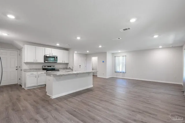 a kitchen with stainless steel appliances kitchen island granite countertop a stove top oven a sink a refrigerator and white cabinets with wooden floor